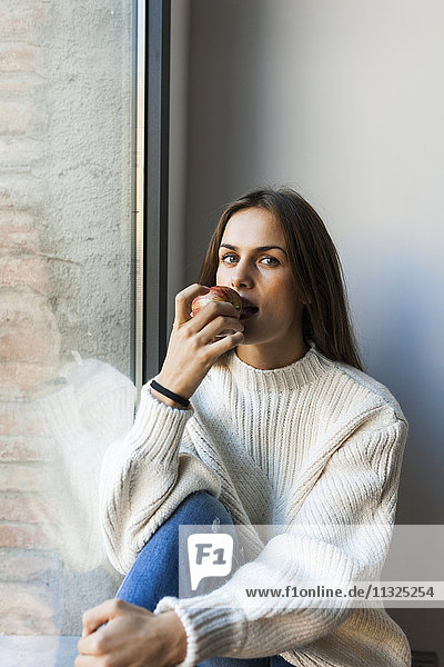 Junge Frau beim Essen eines Apfels am Fenster