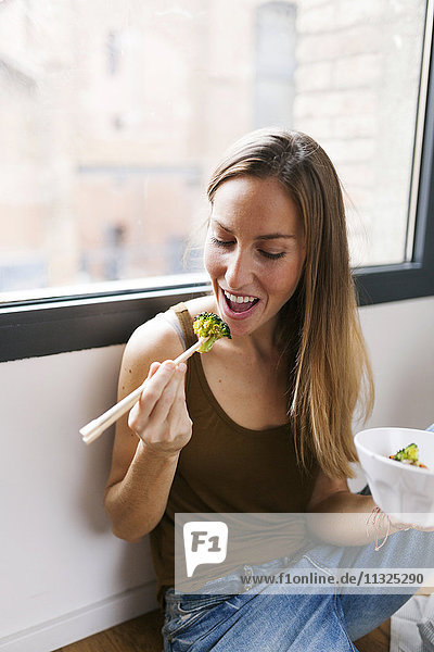 Frau zu Hause beim Essen von Gemüse mit Stäbchen