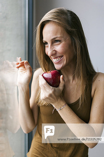 Woman standing by window  eating apple