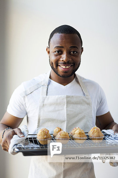 Fröhlicher junger Mann hält Tablett mit Muffins