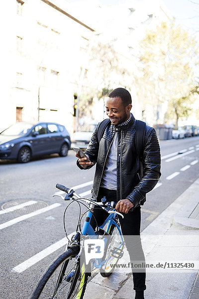 Lächelnder junger Mann mit Fahrrad auf seinem Smartphone