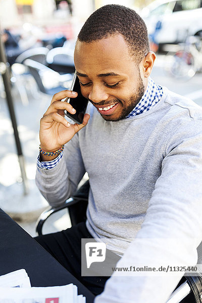 Lächelnder junger Mann am Handy im Straßencafé