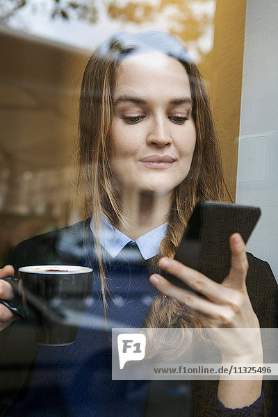 Lächelnde junge Frau im Coffee-Shop mit Tasse Kaffee auf dem Smartphone
