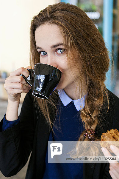 Young woman with muffin drinking cup of coffee