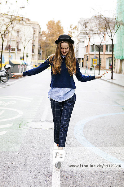Fashionable young woman balancing on median strip of a road