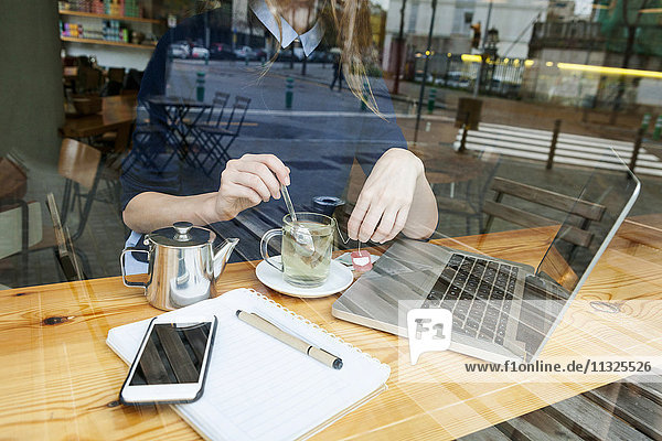 Young woman with laptop and cup of tea in a cafe  partial view