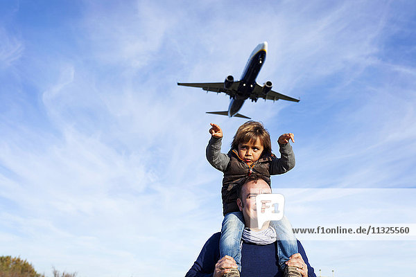 Vater trägt Sohn auf Schultern unter fliegenden Flugzeugen