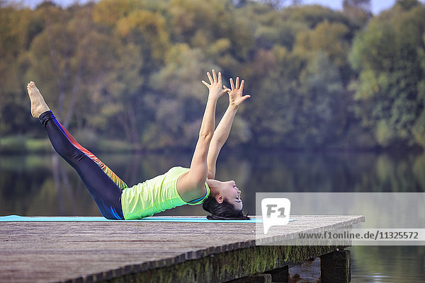 Frau praktiziert Yoga am Steg eines Sees