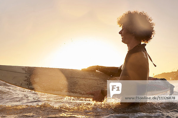 Glücklicher Surfer im Meer bei Sonnenuntergang