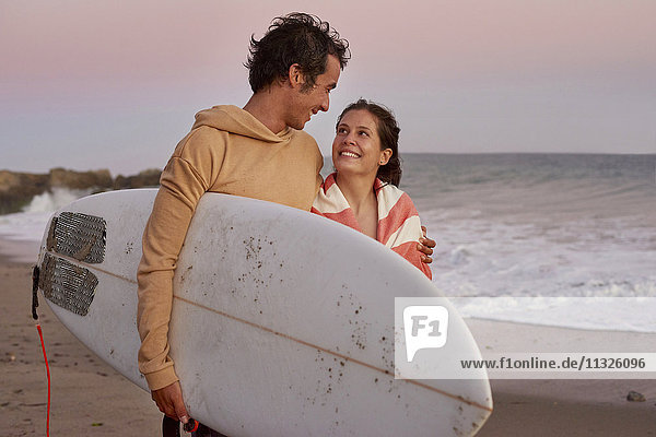 Lächelndes junges Paar mit Surfbrett am Strand