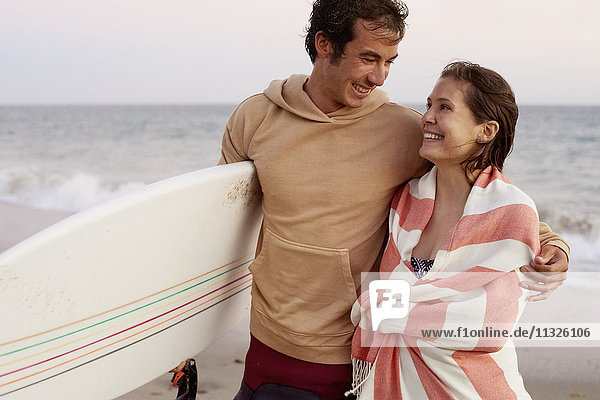 Lächelndes junges Paar mit Surfbrett am Strand
