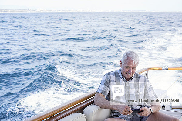 Senior auf einer Bootsfahrt mit Blick auf das Handy