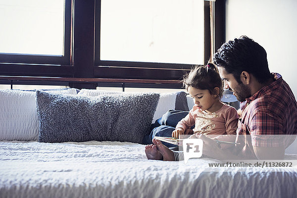 Father and daughter reading book  lying on bed