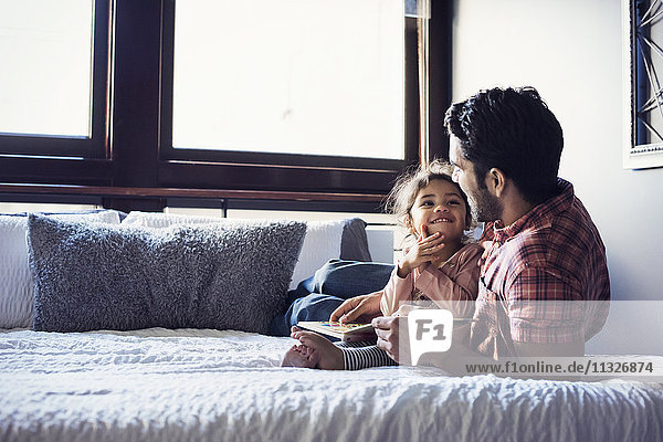 Father and daughter reading book  lying on bed