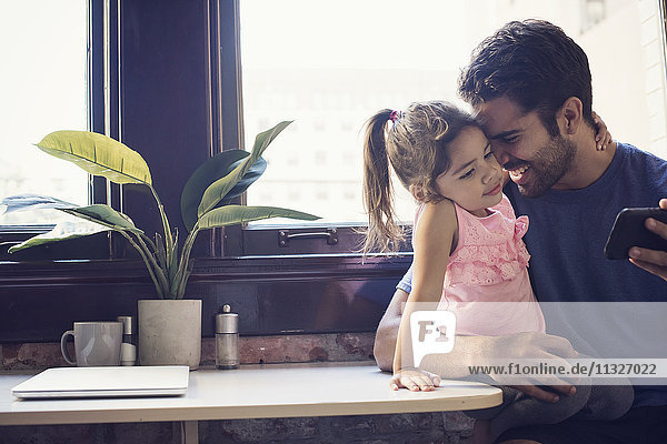Vater mit Tochter mit Smartphone in der Küche