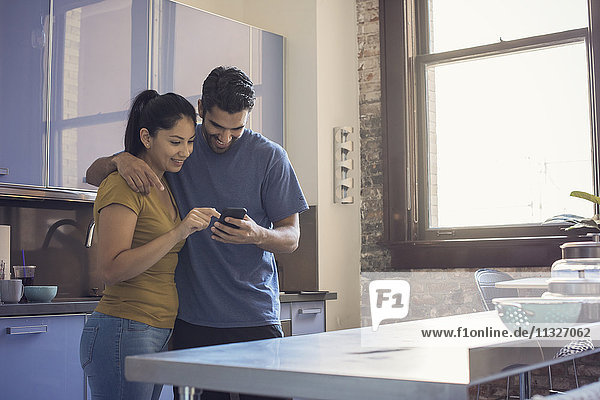 Young couple in kitchen using smart phone