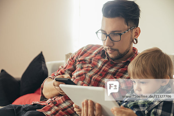Vater und Sohn auf der Couch mit Tablett und Handy