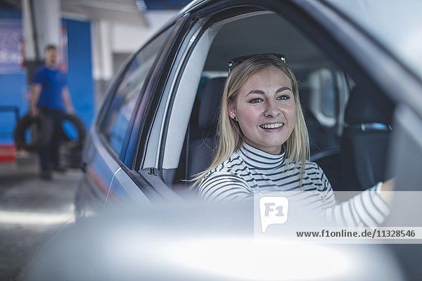 Smiling female customer in car leaving workshop