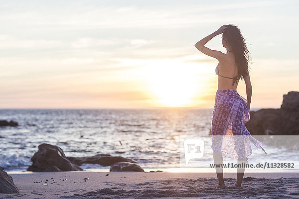Schöne junge Frau im Bikini am Strand bei Sonnenuntergang
