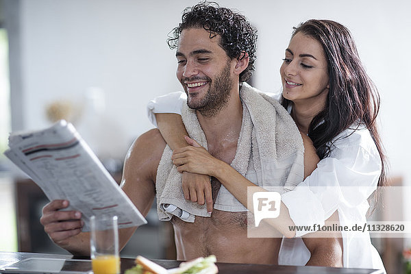 Lächelndes junges Paar zu Hause beim Zeitungslesen
