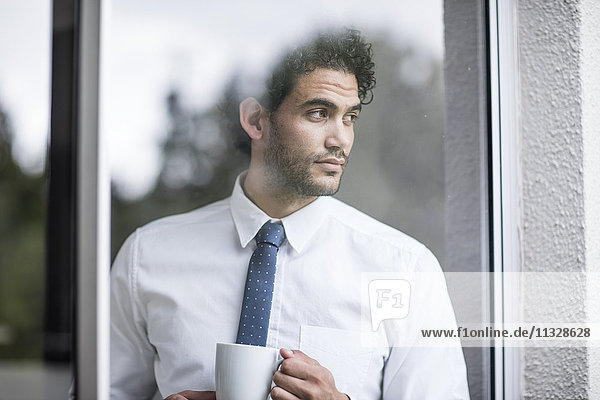 Businessman with cup of coffee looking out of window