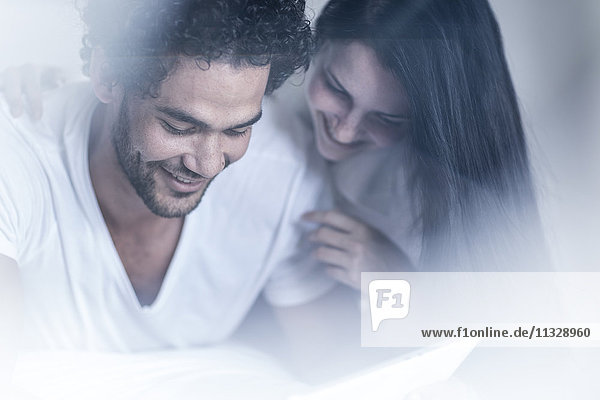 Lächelndes junges Paar im Bett mit Blick auf Tablette