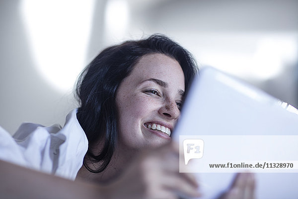 Lächelnde junge Frau im Bett mit Tablette