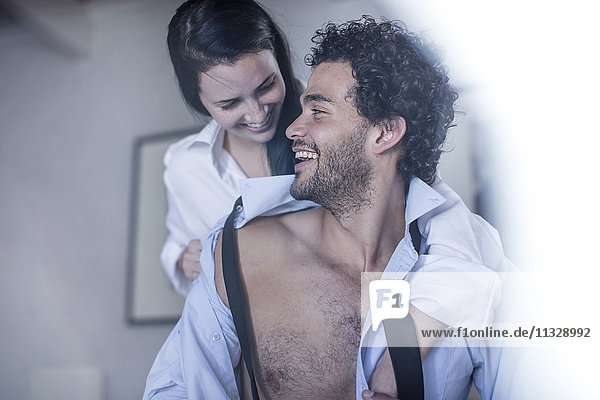 Young man buttoning his shirt while his wife watching him