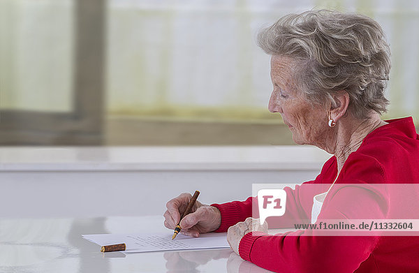 Senior woman writing on a white sheet.