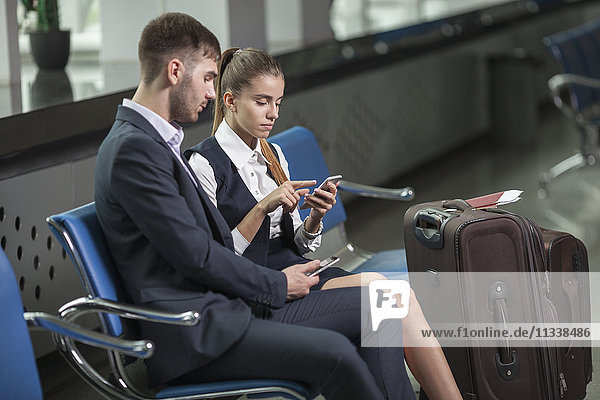 Young business couple using mobile phones while waiting at airport