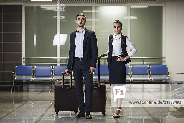 Ganzkörperporträt eines jungen Geschäftsmannes und einer Geschäftsfrau mit Gepäck am Flughafen