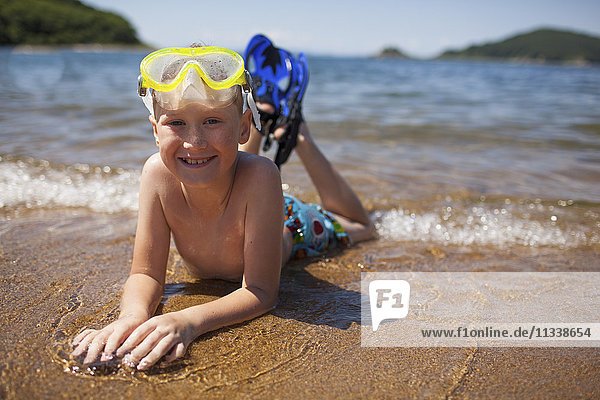 Portrait des Jungen mit Schnorchel und Schwimmbrille am Strand liegend