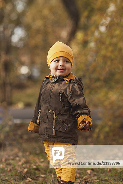 Smiling baby boy looking away while standing in park during autumn