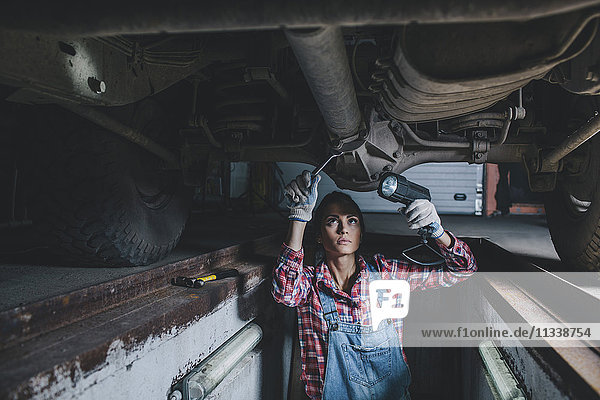 Mechanikerinnen halten die Taschenlampe während der Arbeit unter dem Auto in der Werkstatt.