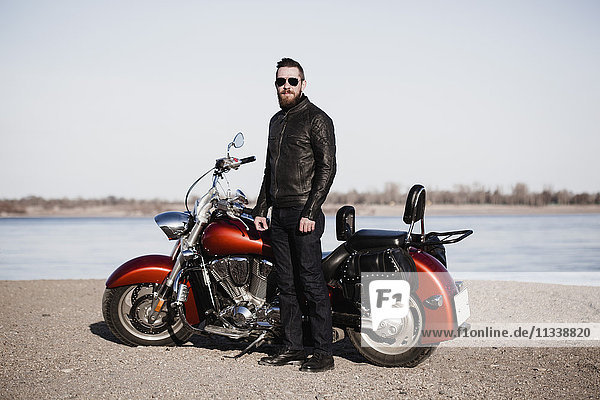 Full length portrait of biker standing by motorcycle at lakeshore