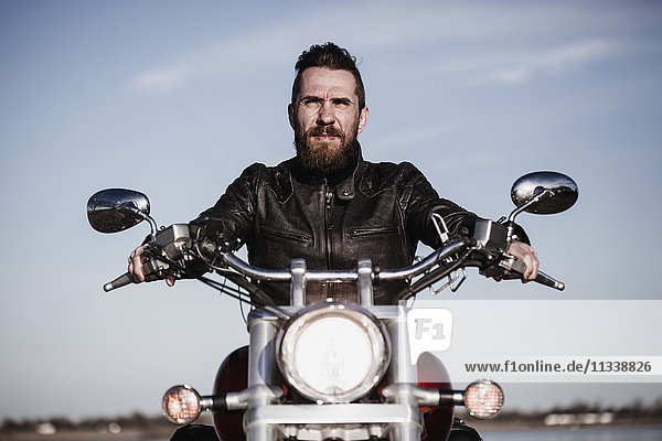 Portrait eines selbstbewussten Bikers  der auf dem Motorrad gegen den Himmel sitzt