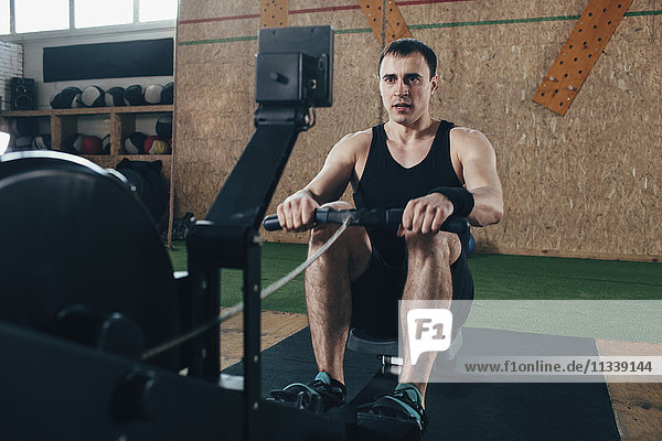 Determined man exercising on rowing machines at gym