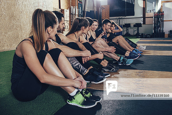Sportlerinnen und Sportler beim Sitzen auf dem Teppich im Fitnessstudio