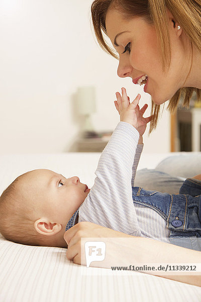 Cute baby boy reaching hands towards mother while lying on bed at home