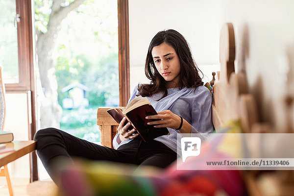 Teenage girl reading book while sitting on sofa