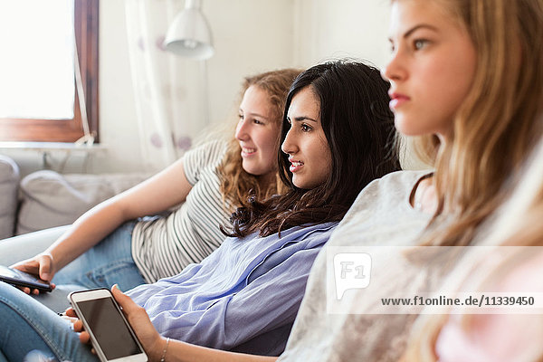 Teenage girls watching TV while relaxing on sofa at home