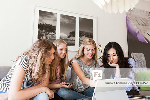 Fröhliche Teenager-Mädchen  die zu Hause auf dem Sofa sitzen und ihren Laptop benutzen.