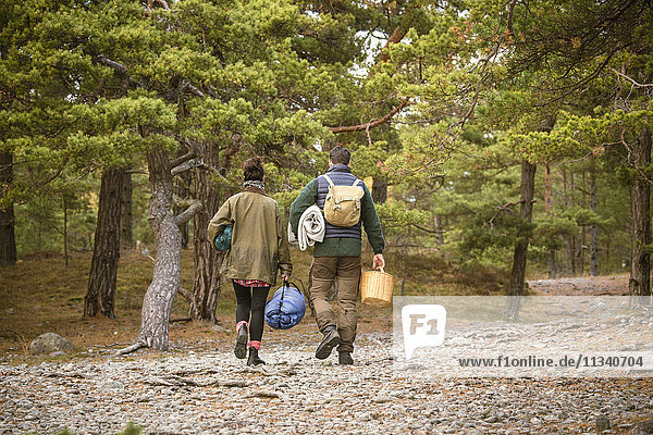 Rear view of couple carrying sleeping bags and basket in forest