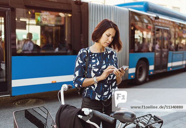 Geschäftsfrau mit Smartphone im Stehen mit dem Fahrrad auf der Stadtstraße