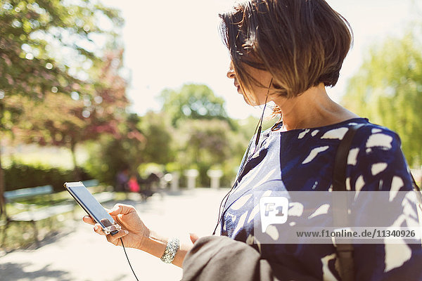 Geschäftsfrau beim Musikhören über Smartphone auf dem Fußweg bei Sonnenschein