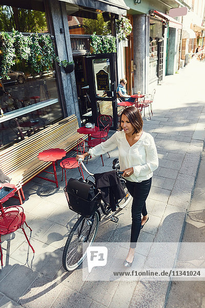 High angle view of businesswoman with bicycle walking on sidewalk