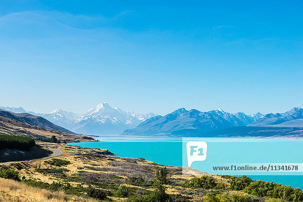 A road winds along the edge of a turquoise blue lake with mountains in the distance  South Island  New Zealand  Pacific