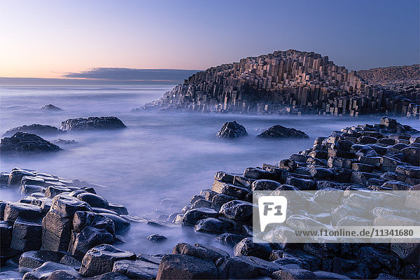 Der Giant's Causeway erhebt sich spät in der Nacht aus dem Atlantik  während das letzte Licht der Sonne hinter dem Horizont verschwindet  County Antrim  Nordirland  Vereinigtes Königreich  Europa