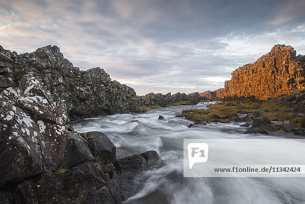 Ein Fluss fließt vom Oxarafoss-Wasserfall bei Sonnenaufgang im Thingvellir-Nationalpark  UNESCO-Welterbe  Island  Polarregionen