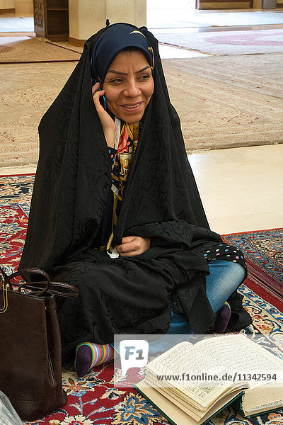 Junge Frau  hin- und hergerissen zwischen ihrem Handy und ihrer religiösen Lektüre  Aramgah-e Shah-e Cheragh (Mausoleum des Königs des Lichts)  Shiraz  Iran  Naher Osten
